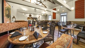 A spacious dining area with high ceilings, exposed beams, and modern pendant lighting. Tables are set with fine china, glassware, and napkins. - The Shaw Club Hotel (Niagara-on-the-Lake)