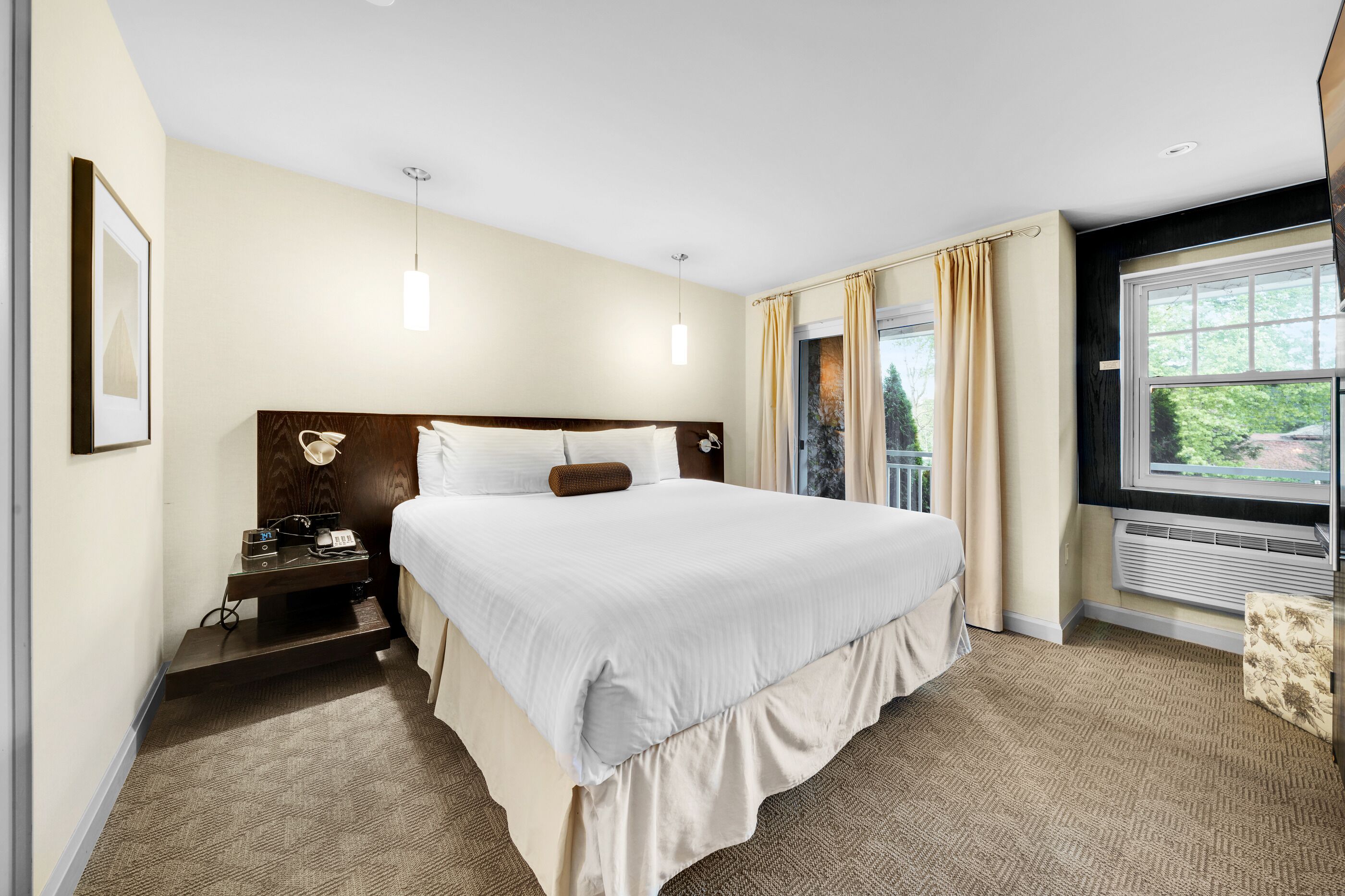 A hotel room with a large bed, bedside table, lamp, and a window with curtains.