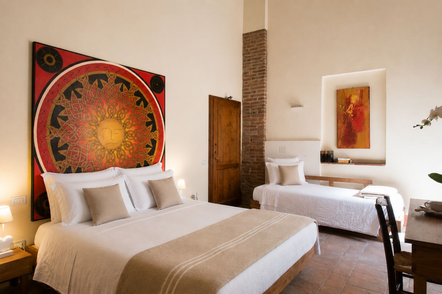 Een hotelkamer met twee bedden, een groot wandtapijt en een bakstenen muur.