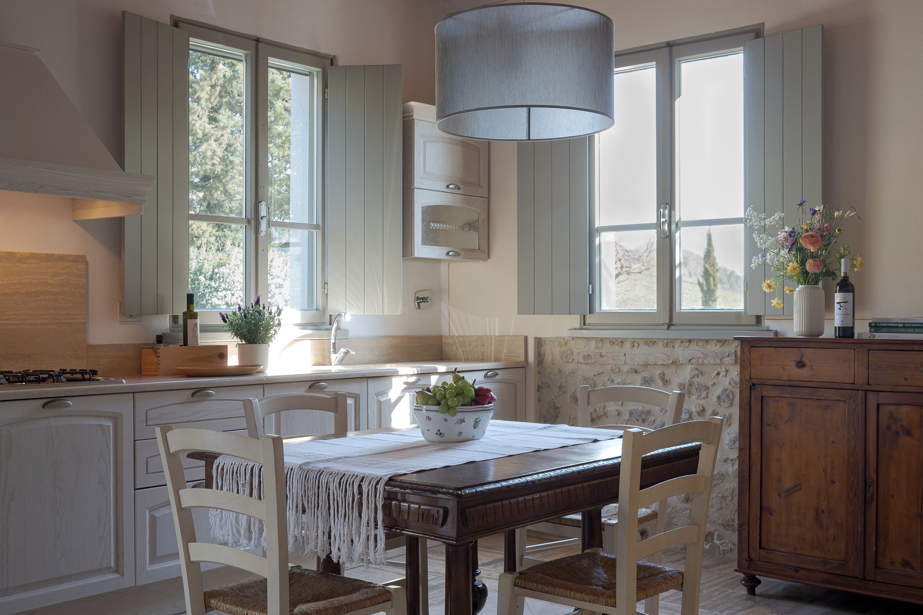 Una cocina con mesa, sillas, lámpara colgante y ventana con vista a árboles.