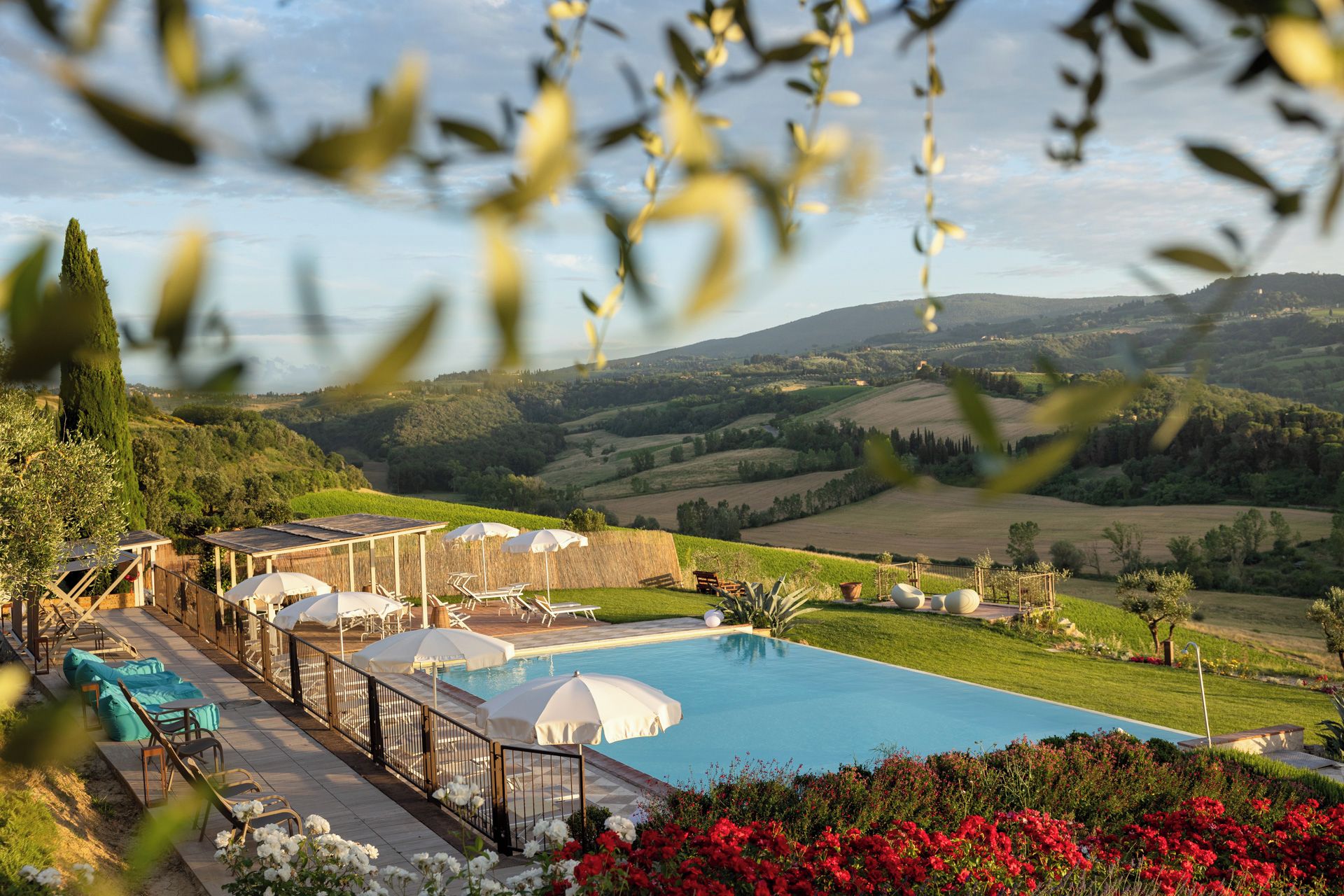 A poolside area with lounge chairs and umbrellas, surrounded by a landscaped garden with red flowers.