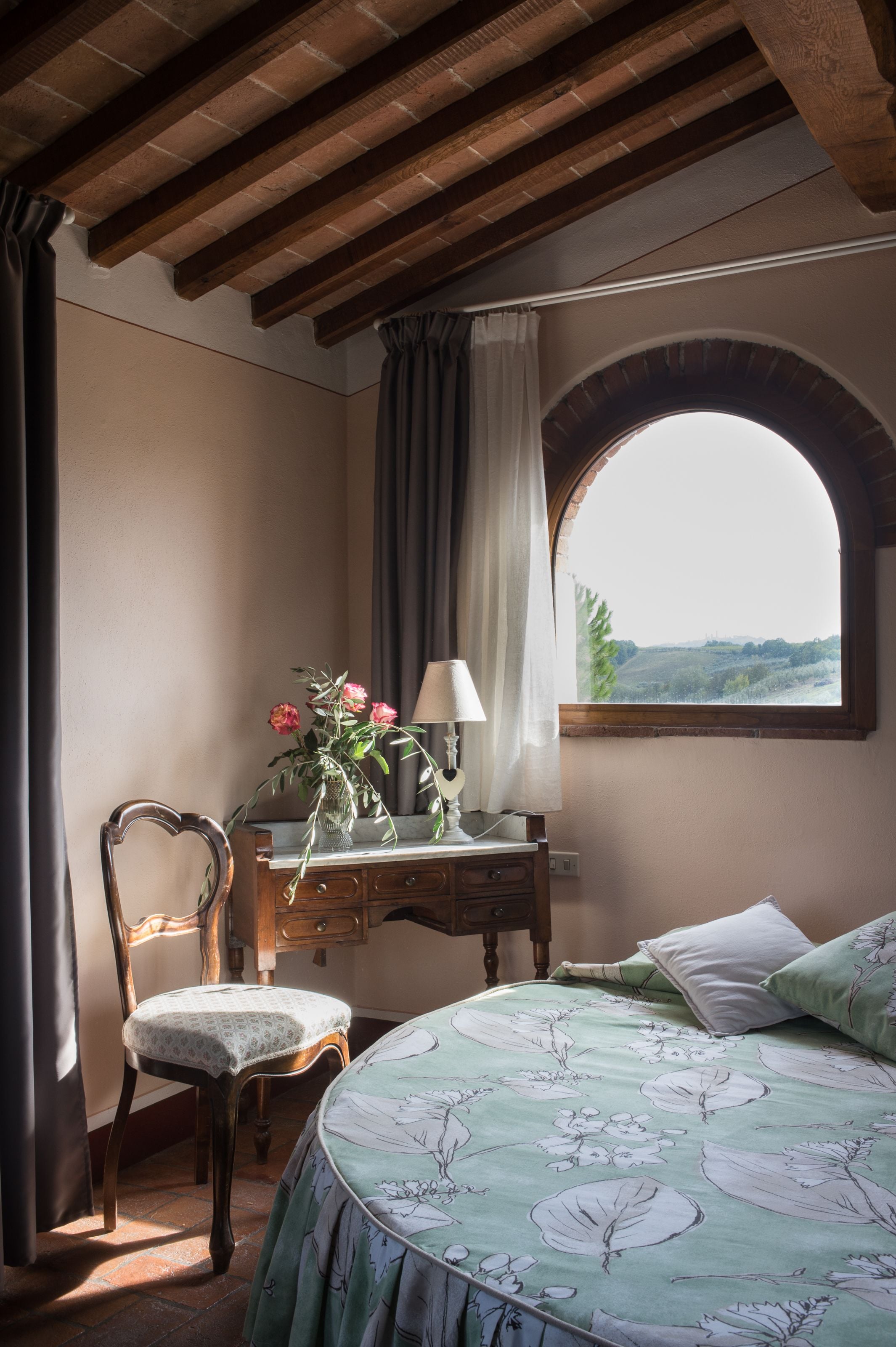 A bedroom with a bed, a chair, a desk, and a window with a view.