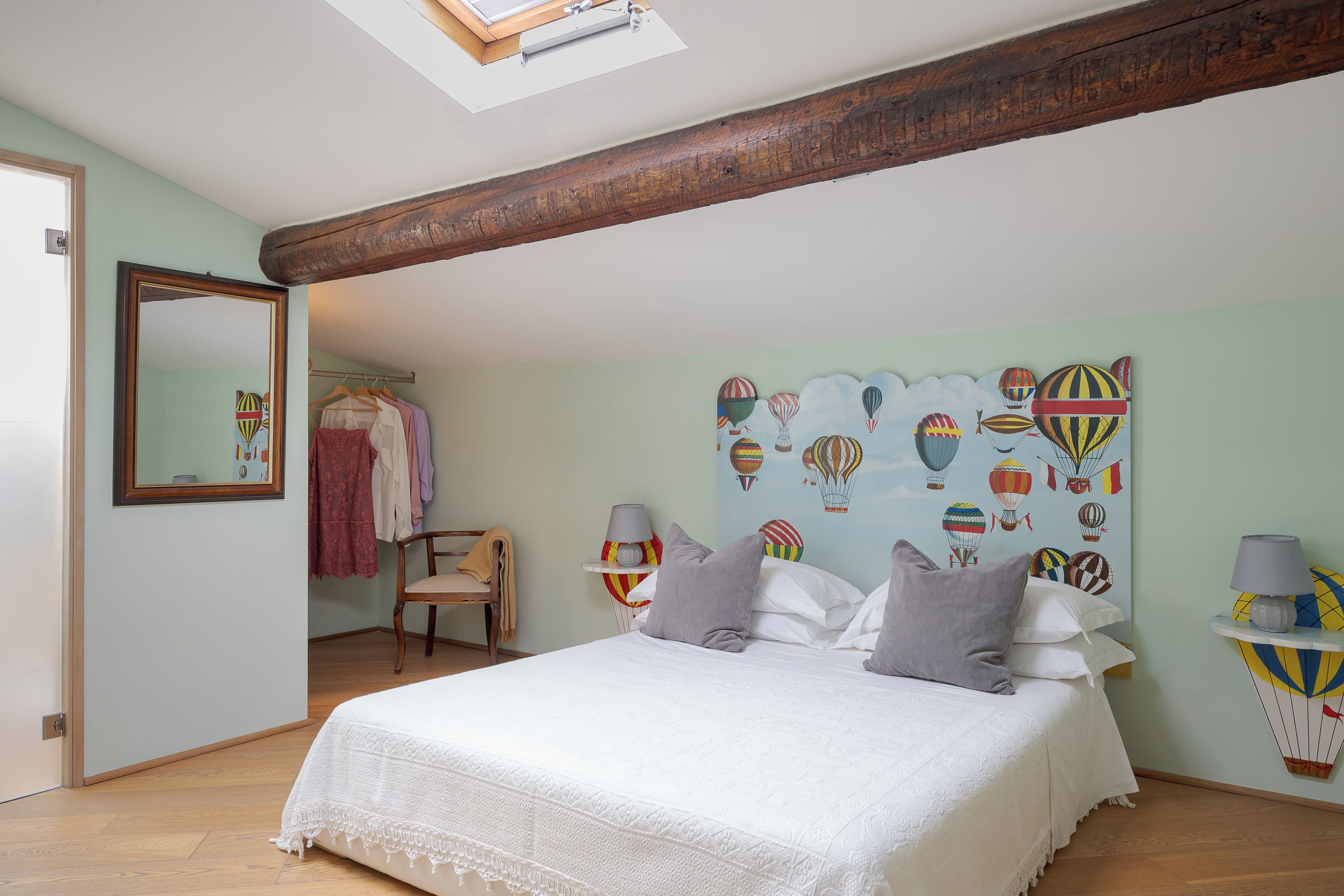 A bedroom with a bed, a hanging chair, a wardrobe, and a wall with a hot air balloon mural.