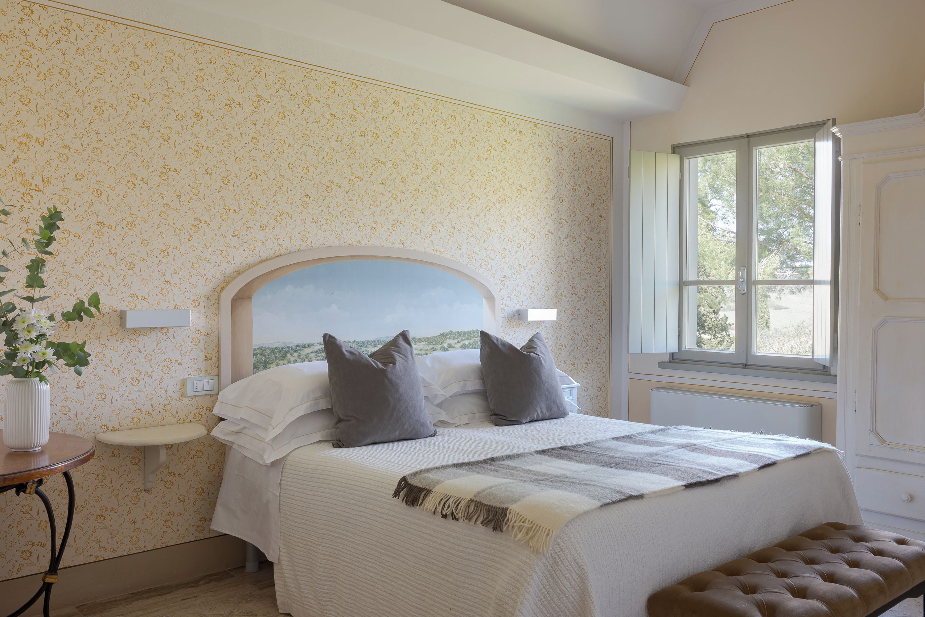 A bedroom with a bed, a bedside table, a window, and a view of the outdoors.