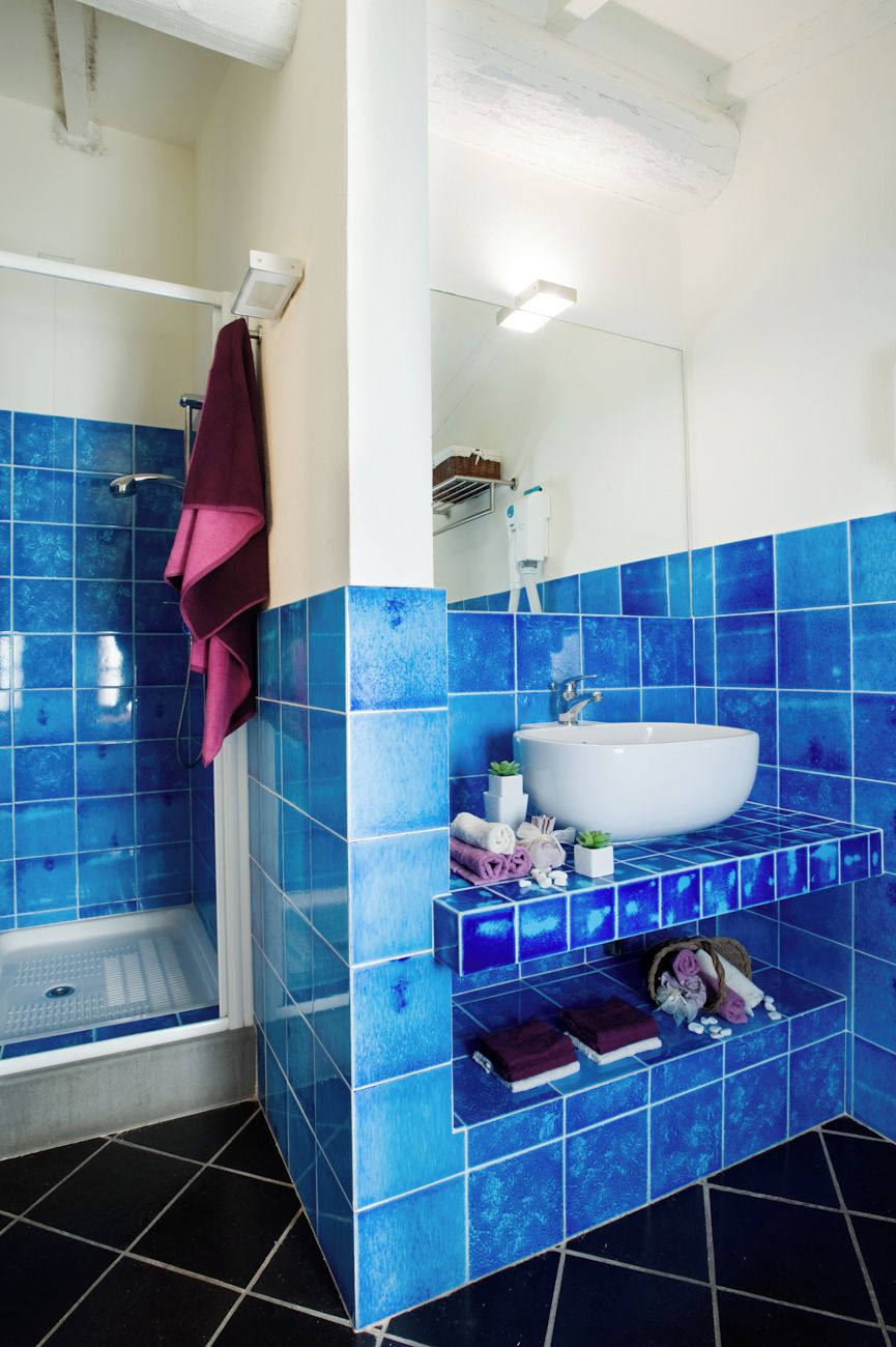 Un baño con azulejos azules, un lavamanos blanco, un espejo y una zona de ducha.