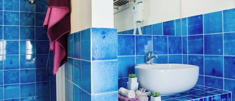 Un baño con azulejos azules, un lavamanos blanco, un espejo y una zona de ducha.