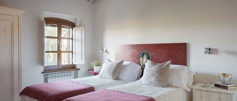 Un dormitorio con cama, mesita de noche, ventana y radiador.