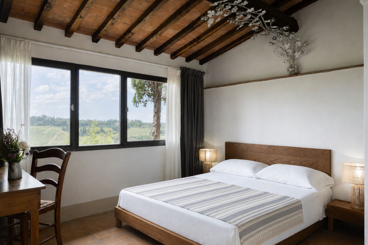 Quarto com cama de madeira, mesa de cabeceira, abajur, cadeira, mesa e vista para o exterior pela janela.