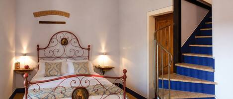 A bedroom with a metal-framed bed, two bedside lamps, a wooden headboard, and a blue staircase with a wooden railing.