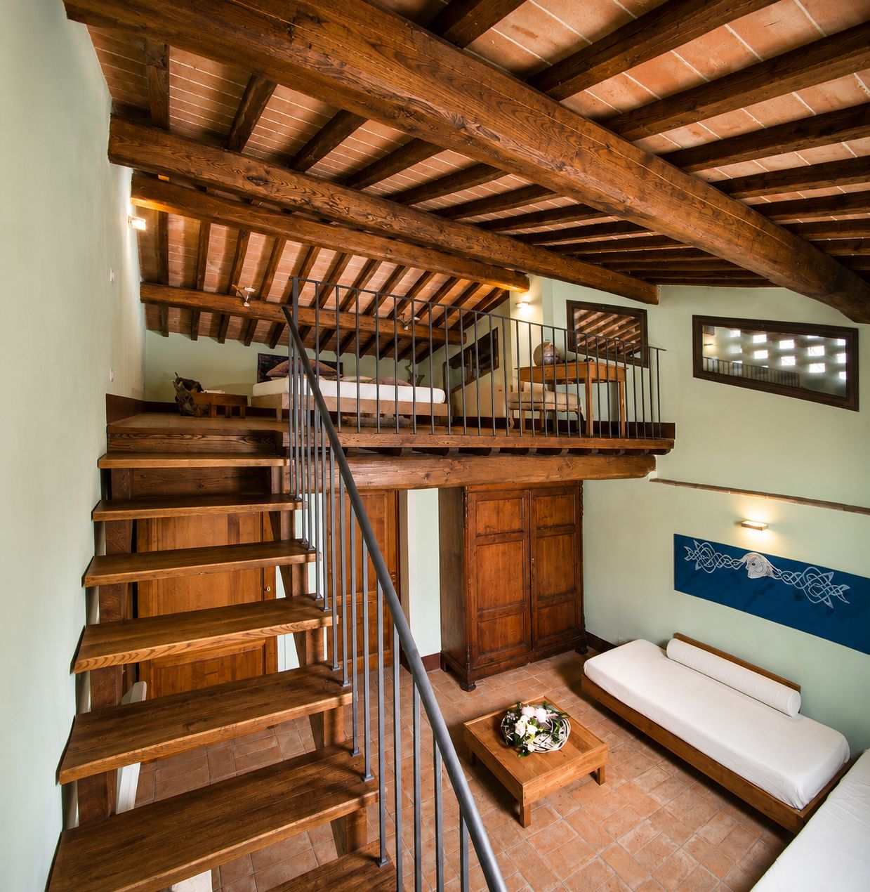 Una escalera de madera que conduce a un nivel superior con un balcón, un sofá y un adorno en la pared.
