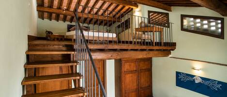 Una escalera de madera que conduce a un nivel superior con un balcón, un sofá y un adorno en la pared.