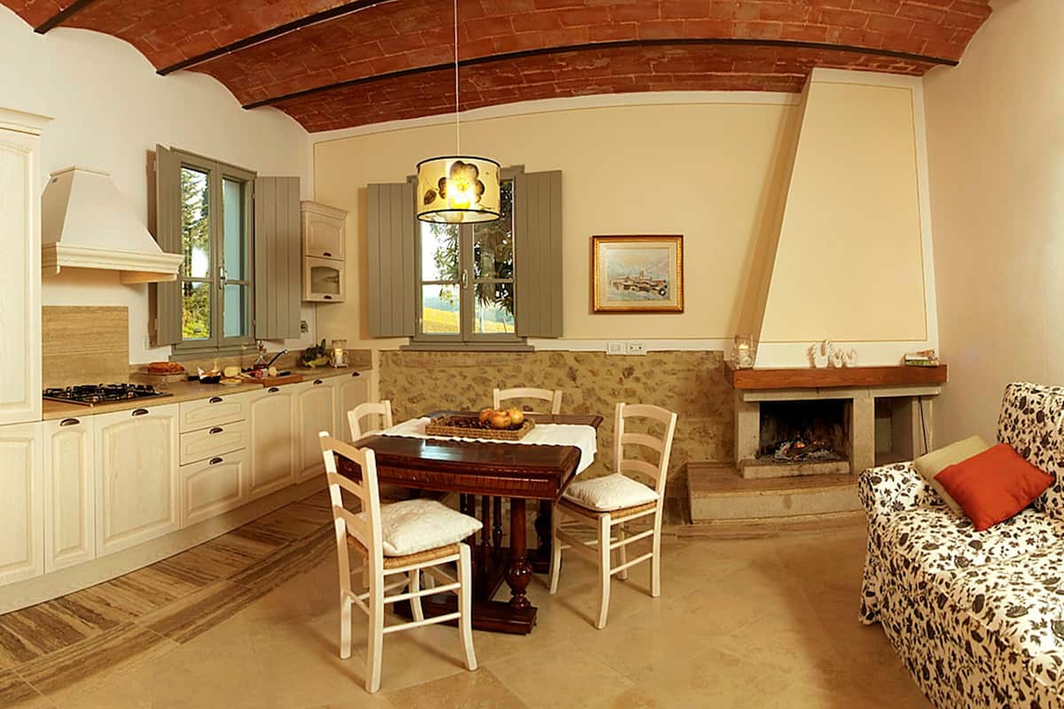 A cozy kitchen with white cabinetry, a dining table with chairs, a hanging light fixture, and a fireplace.