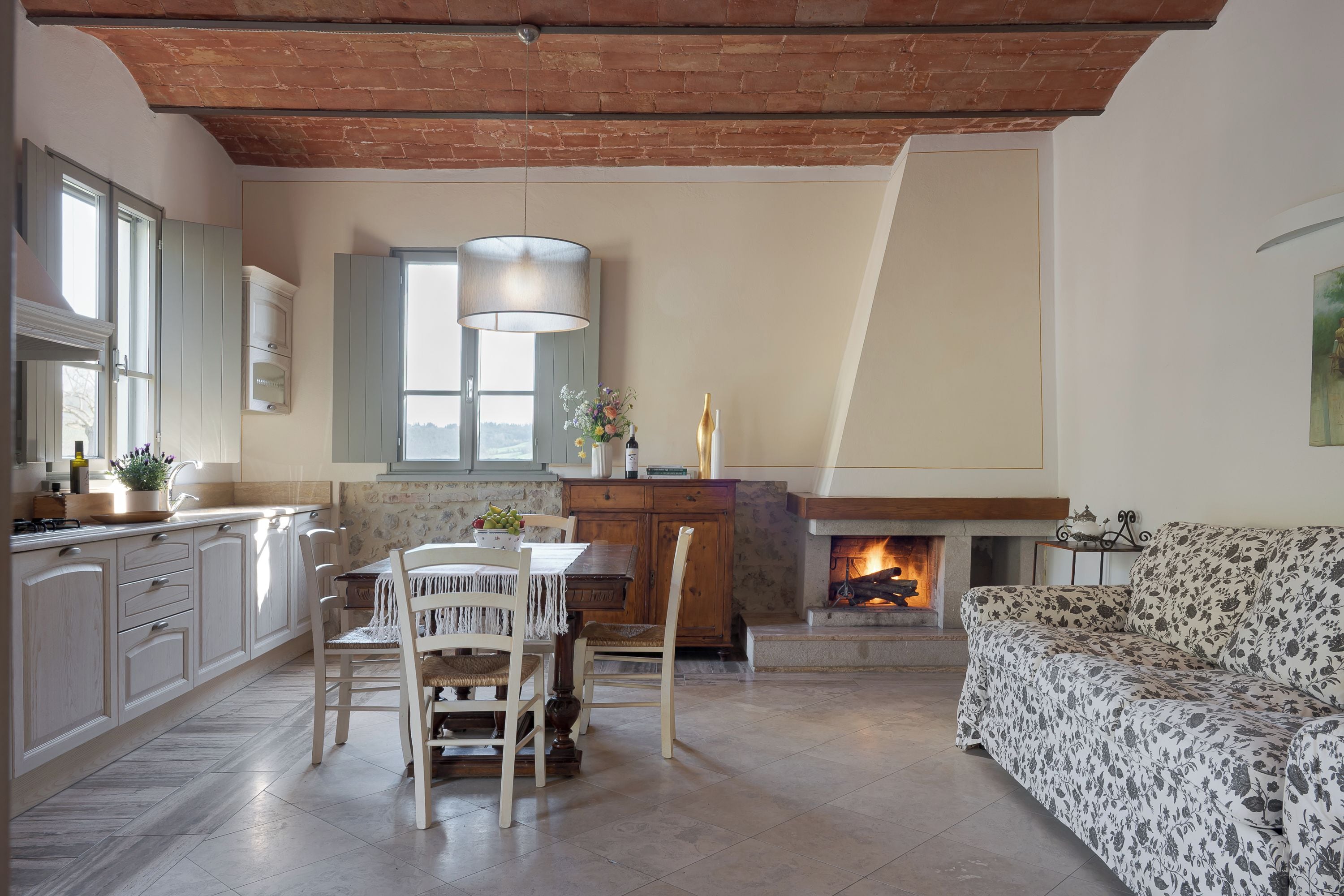 Un salon confortable avec une cheminée, un coin repas avec une table et des chaises, et une cuisine équipée de placards et dotée d’une fenêtre.
