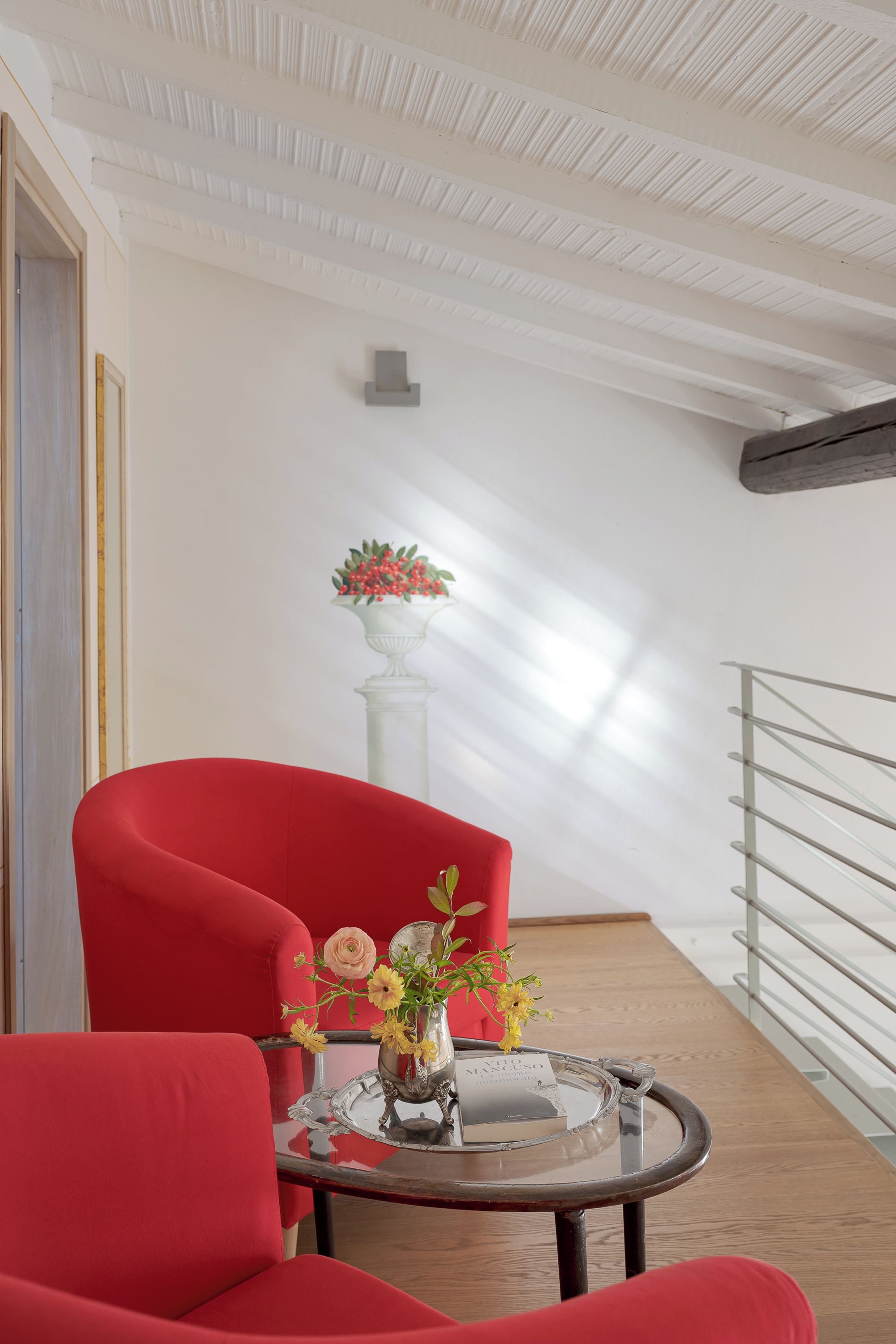 Un interior moderno con una silla roja, una mesa de vidrio con un jarrón de flores y un pilar blanco con una planta.