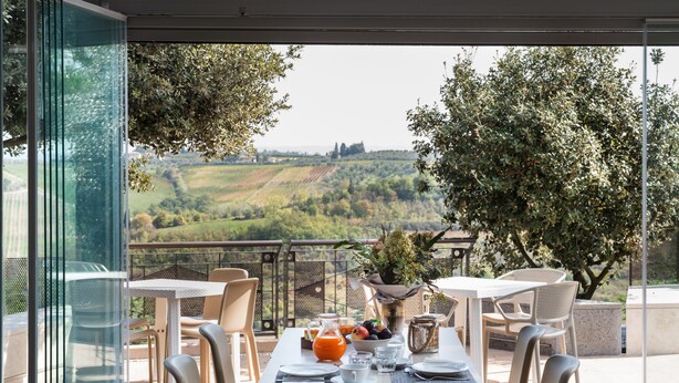 A dining area with a table set for four, overlooking a scenic landscape. - Poderi Arcangelo (San Gimignano)