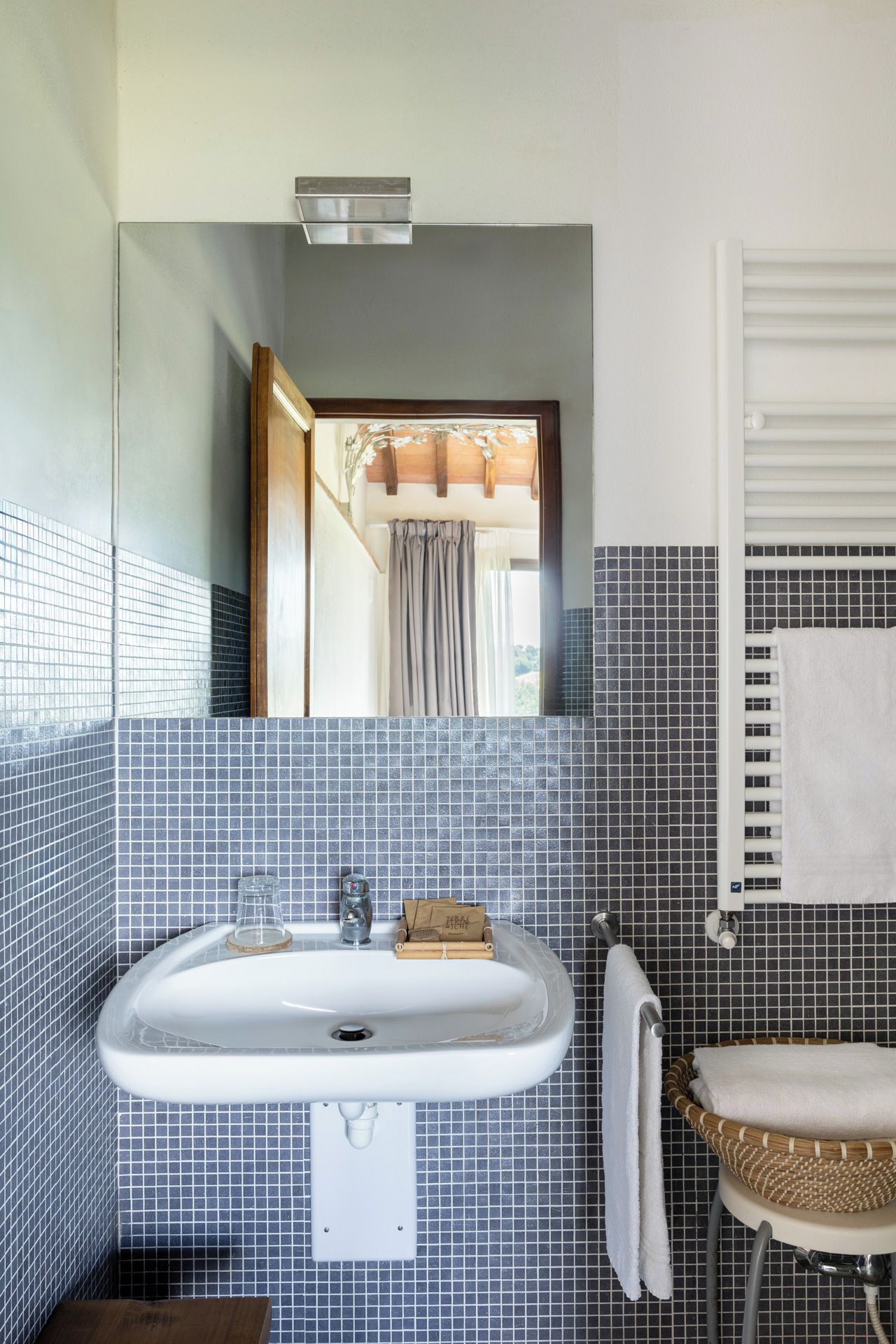 A bathroom with a white sink, a mirror, a towel rack, and a window with curtains.