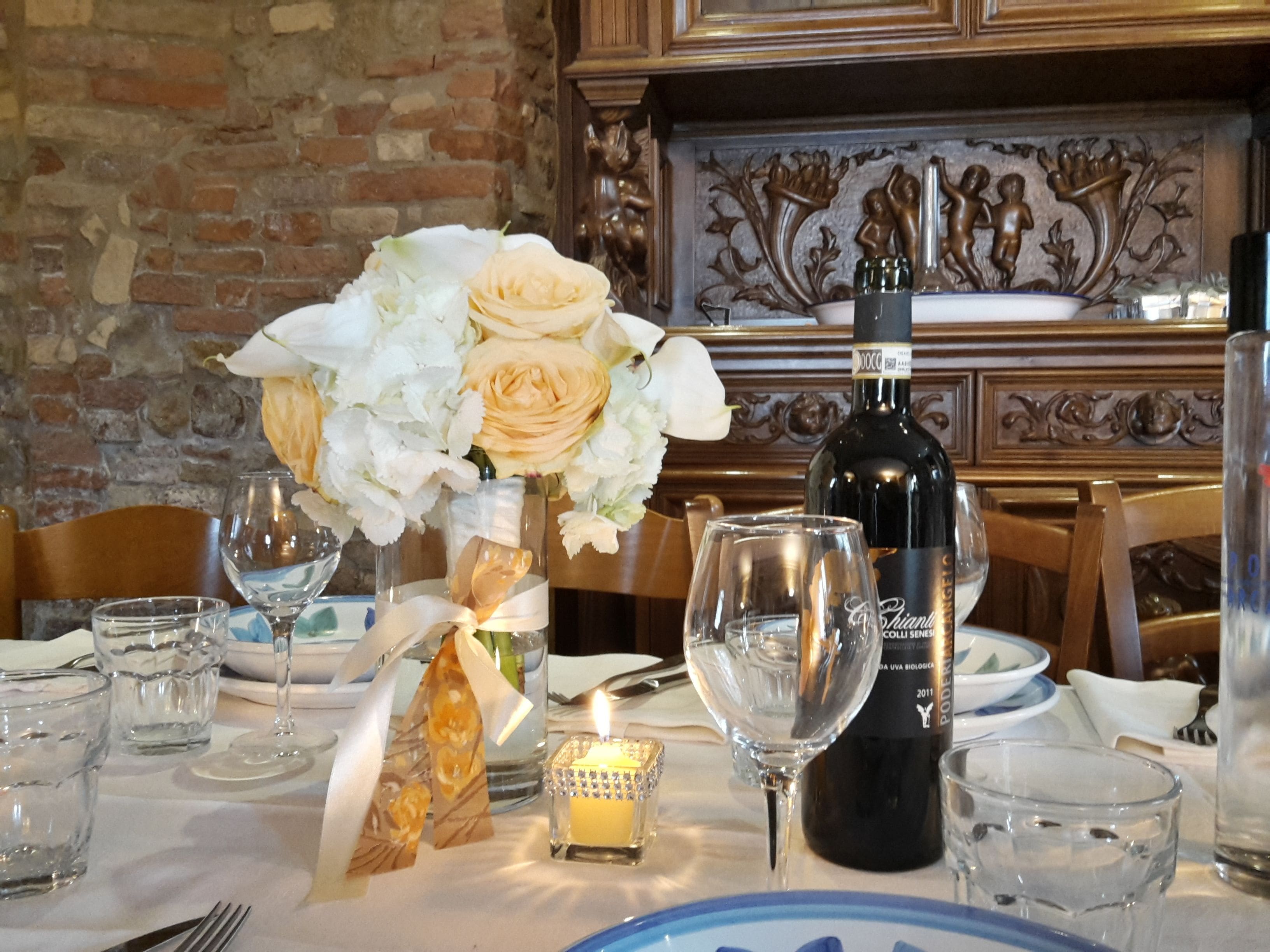 Una mesa de comedor lista con copas de vino, una vela y una botella de vino.