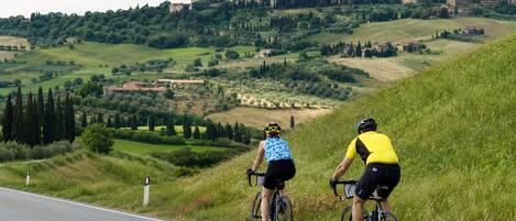 Two cyclists on a road with a view of a hilltop town and castle in the background.