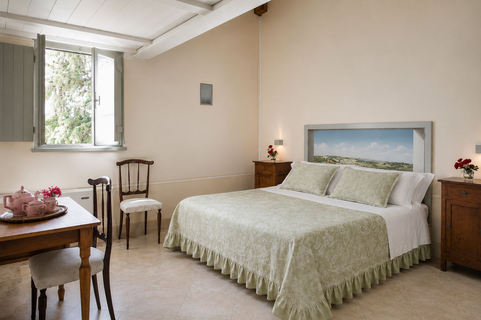 A bedroom with a bed, a chair, a table with a tea set, and a window with a view of greenery.