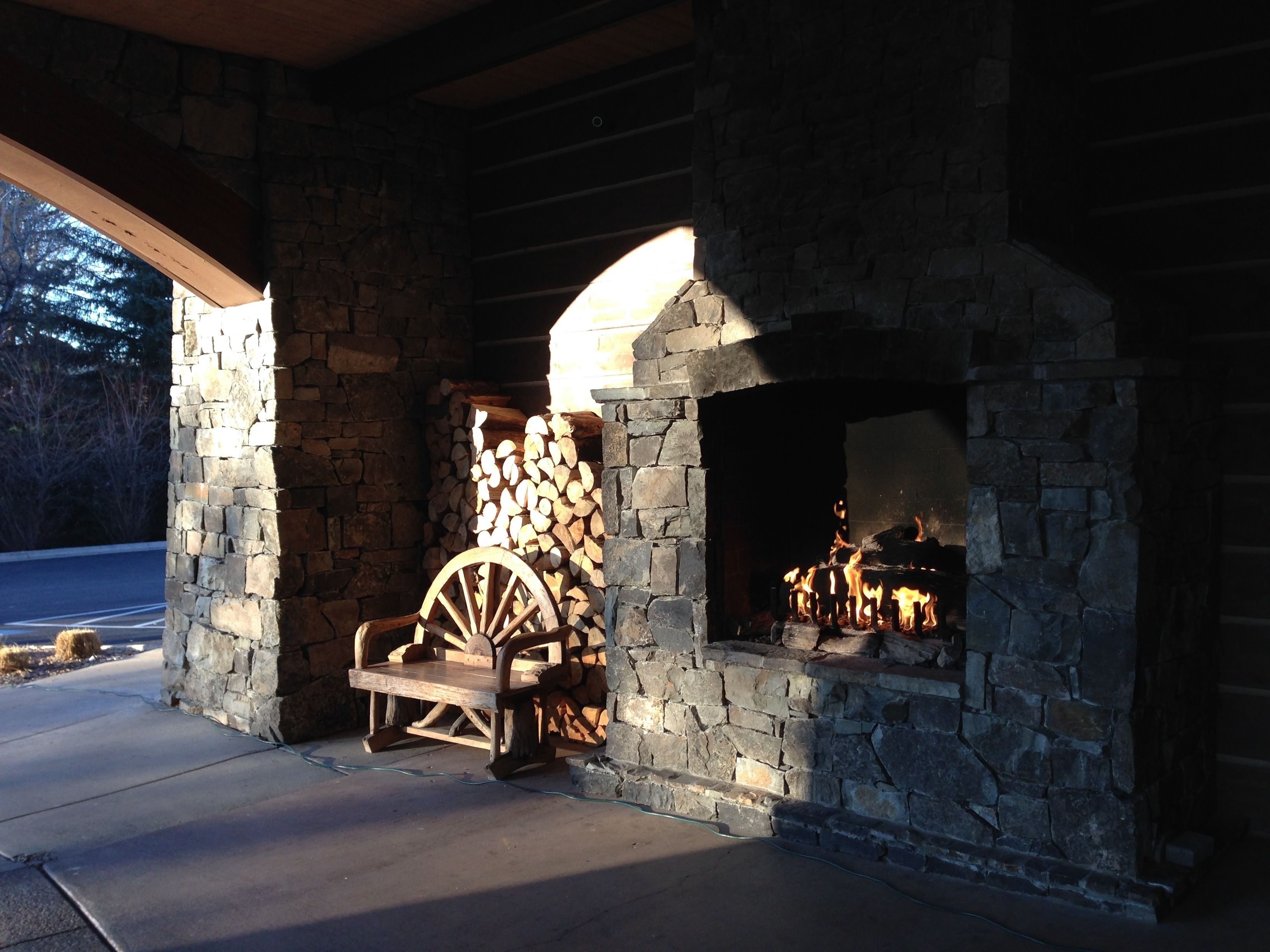 A stone fireplace with a wooden log storage area and a wooden cart.