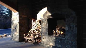 A stone fireplace with a wooden log storage area and a wooden cart.
