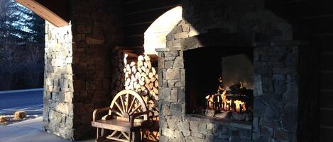 A stone fireplace with a wooden log storage area and a wooden cart.