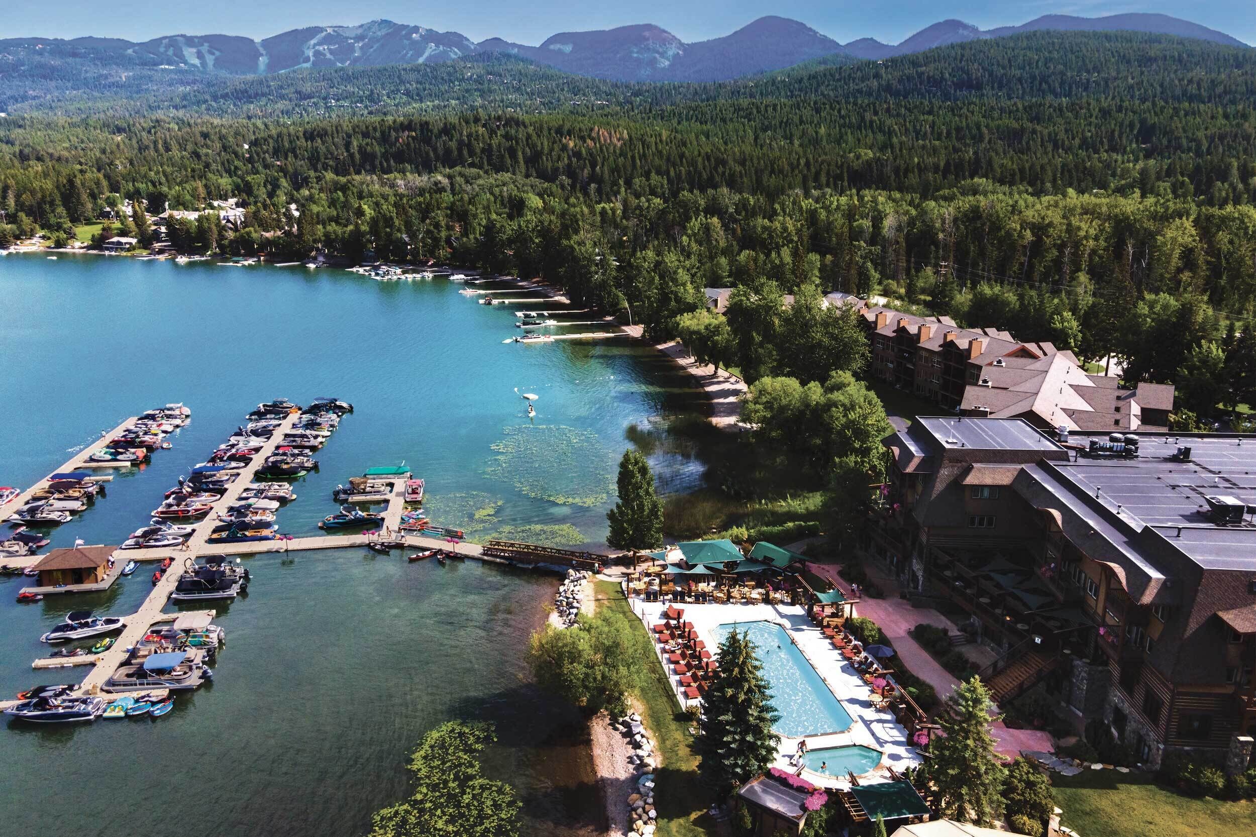 Un complexe hôtelier au bord d’un lac, doté d’un port de plaisance, d’une piscine et offrant une vue sur les montagnes.