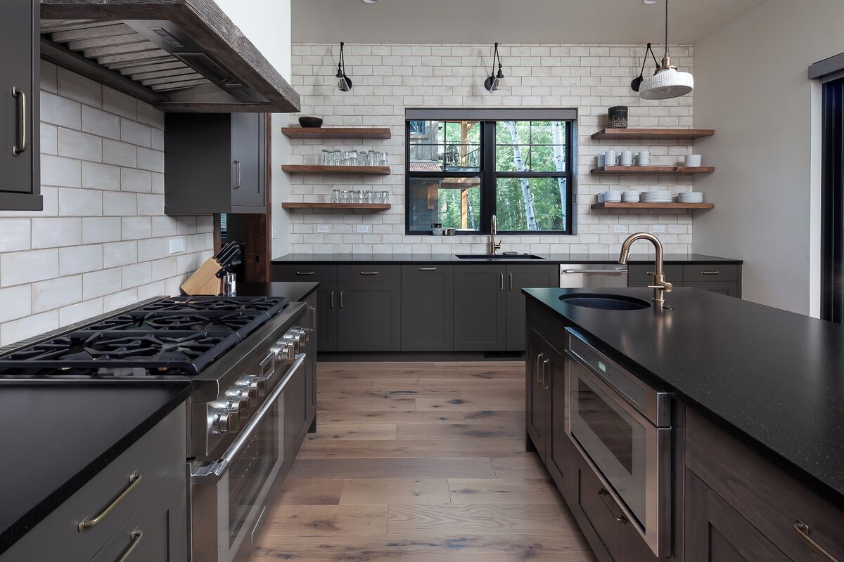 A modern kitchen with dark cabinetry, a black countertop, and a window with a view of trees.