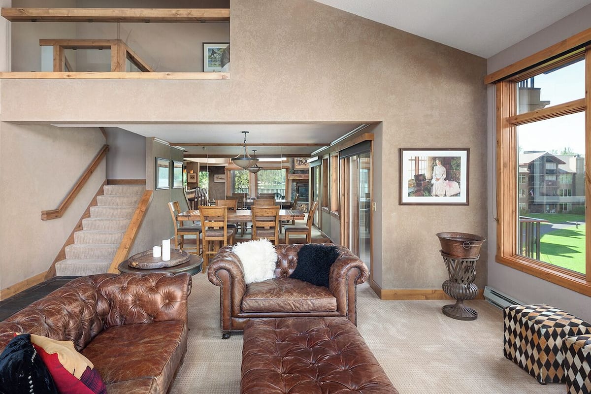 A spacious living room with leather sofas, a dining area, and a staircase leading to an upper level.