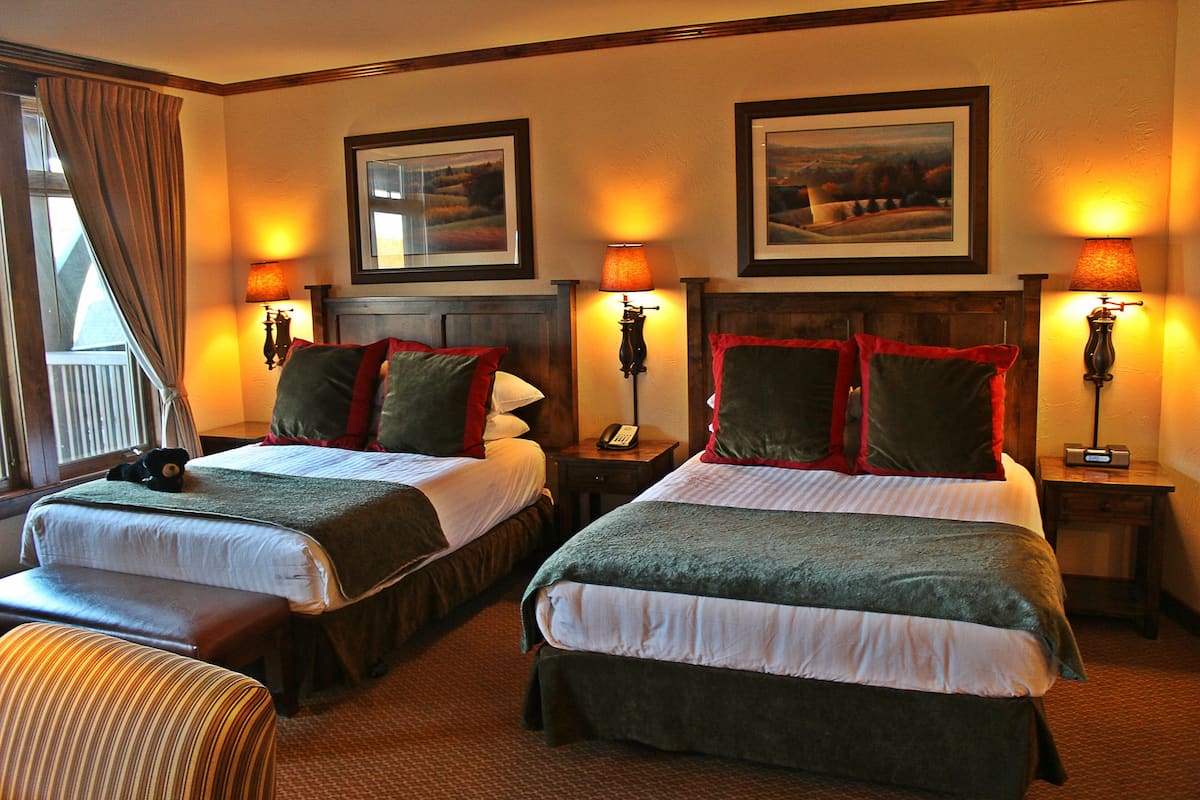 A hotel room with two beds, a bench, a telephone, and framed pictures on the wall.