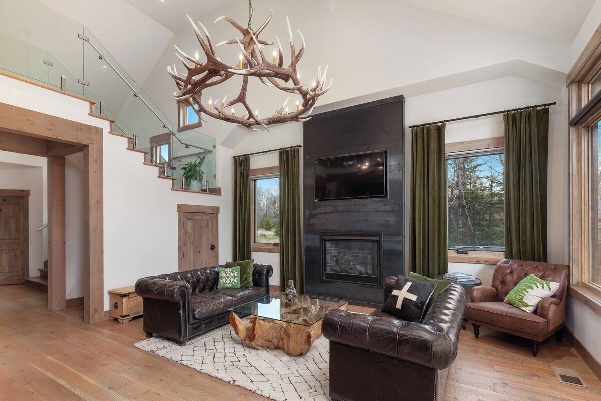 A modern living room with a fireplace, leather sofas, a glass coffee table, and a large chandelier.