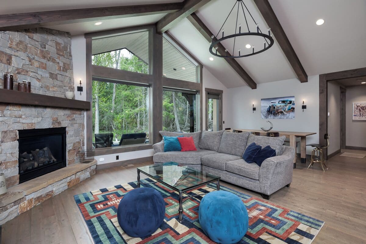 A modern living room with a stone fireplace, large windows, a gray sofa, and a glass coffee table.