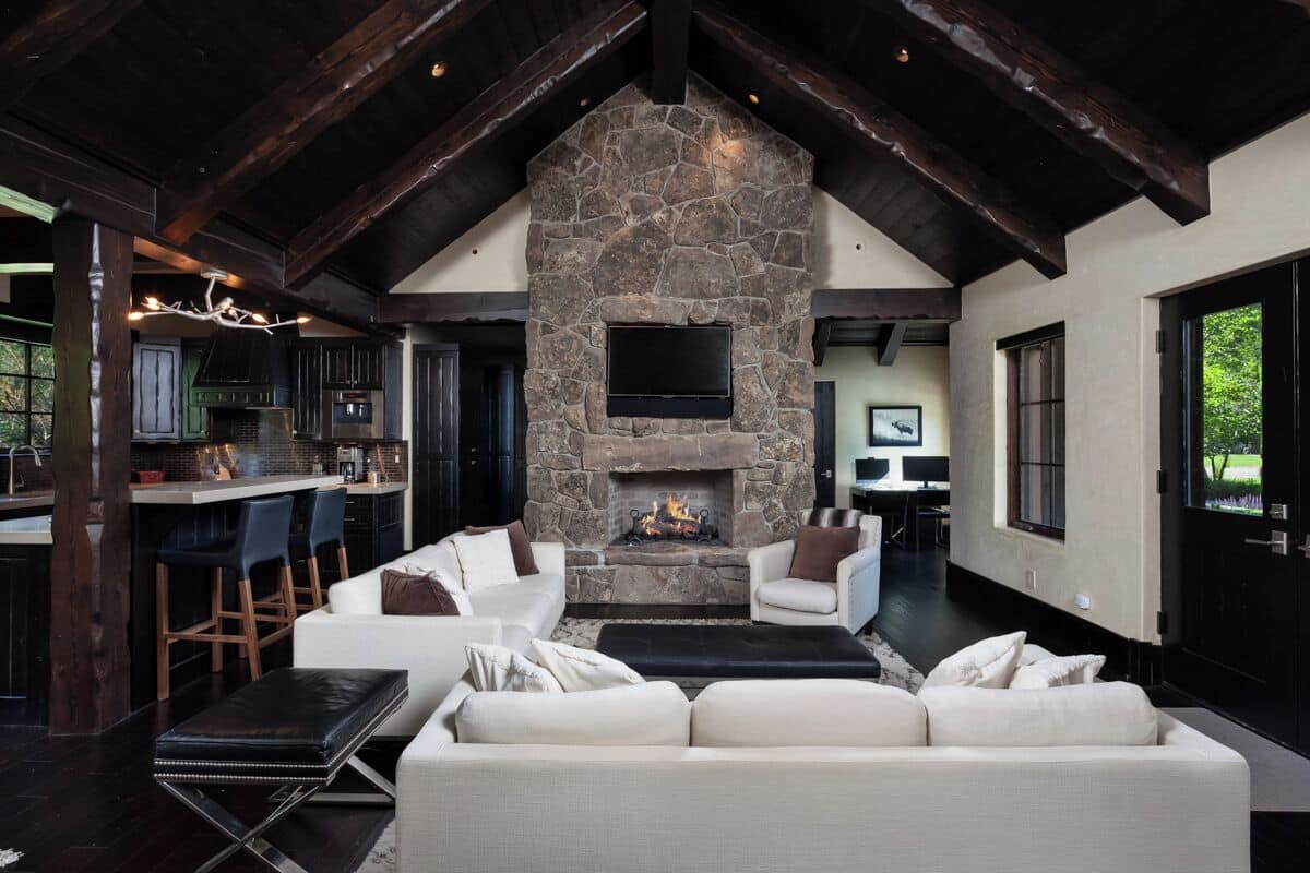 A modern living room with a stone fireplace, white sofas, and a bar area with stools.