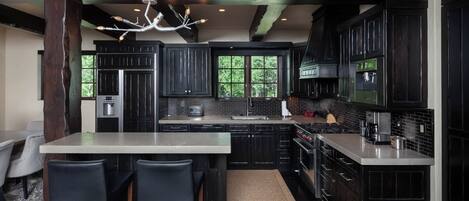 A modern kitchen with dark cabinetry, a central island with bar stools, and a chandelier.