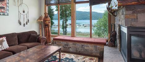 Ein gemütliches Wohnzimmer mit großem Fenster mit Seeblick, einem Kamin aus Stein und rustikaler Einrichtung.