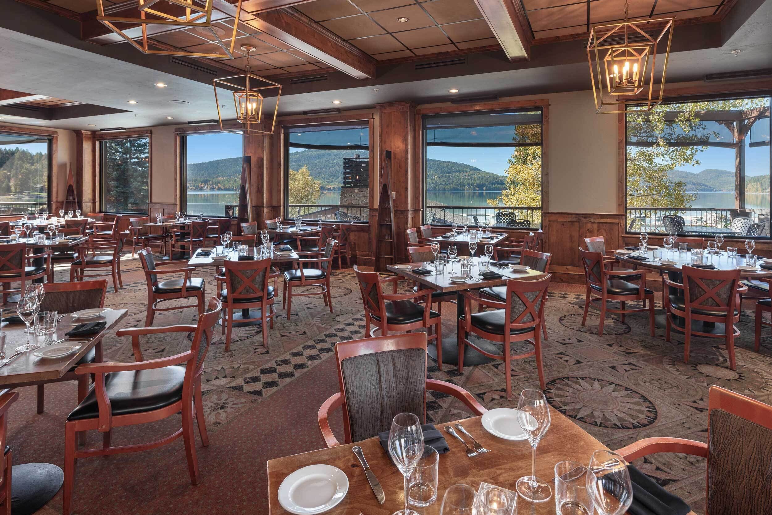 Ein Restaurant mit mehreren Tischen und Stühlen, großen Fenstern mit Bergblick und einer Holzinnenausstattung.