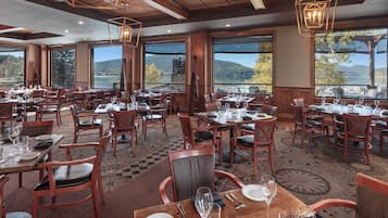 Ein Restaurant mit mehreren Tischen und Stühlen, großen Fenstern mit Bergblick und einer Holzinnenausstattung.
