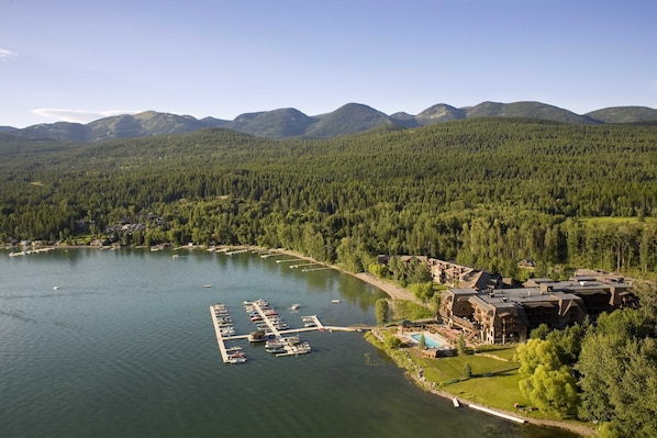 A lodge with a dock and boats, surrounded by forested mountains and a lake.