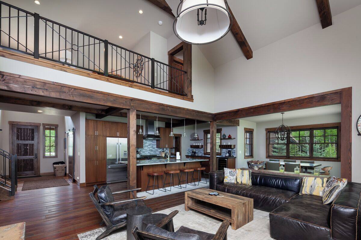 A spacious living area with a high ceiling, wooden beams, a large sofa, leather chairs, a coffee table, and a kitchen area with a bar.
