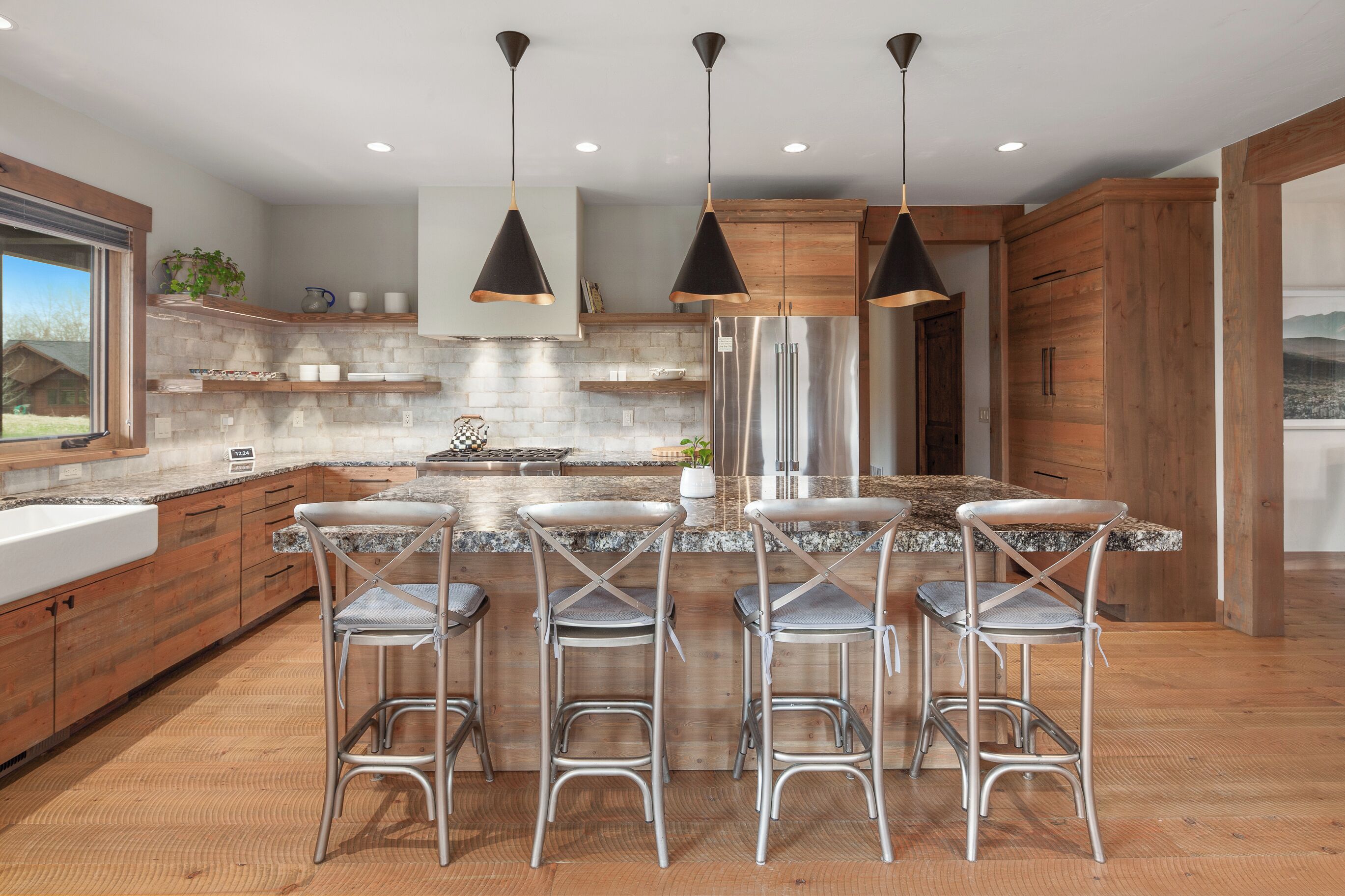 Una cocina moderna con una isla central, taburetes de bar, electrodomésticos de acero inoxidable y armarios de madera.