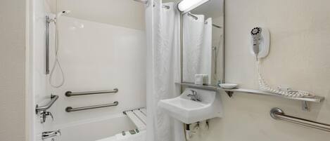 A modern bathroom with a bathtub, shower, and a hairdryer mounted on the wall.