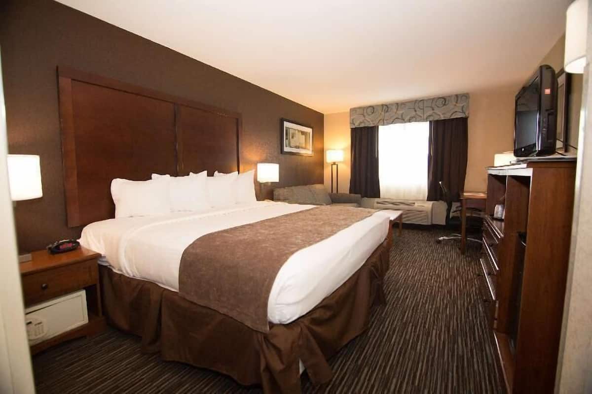 A hotel room with a large bed, a desk with a chair, a television, and a lamp.