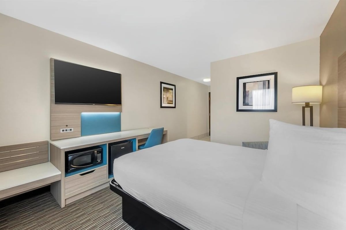 Een hotelkamer met een bed, een bureau met een flatscreen televisie, een magnetron en een lamp.