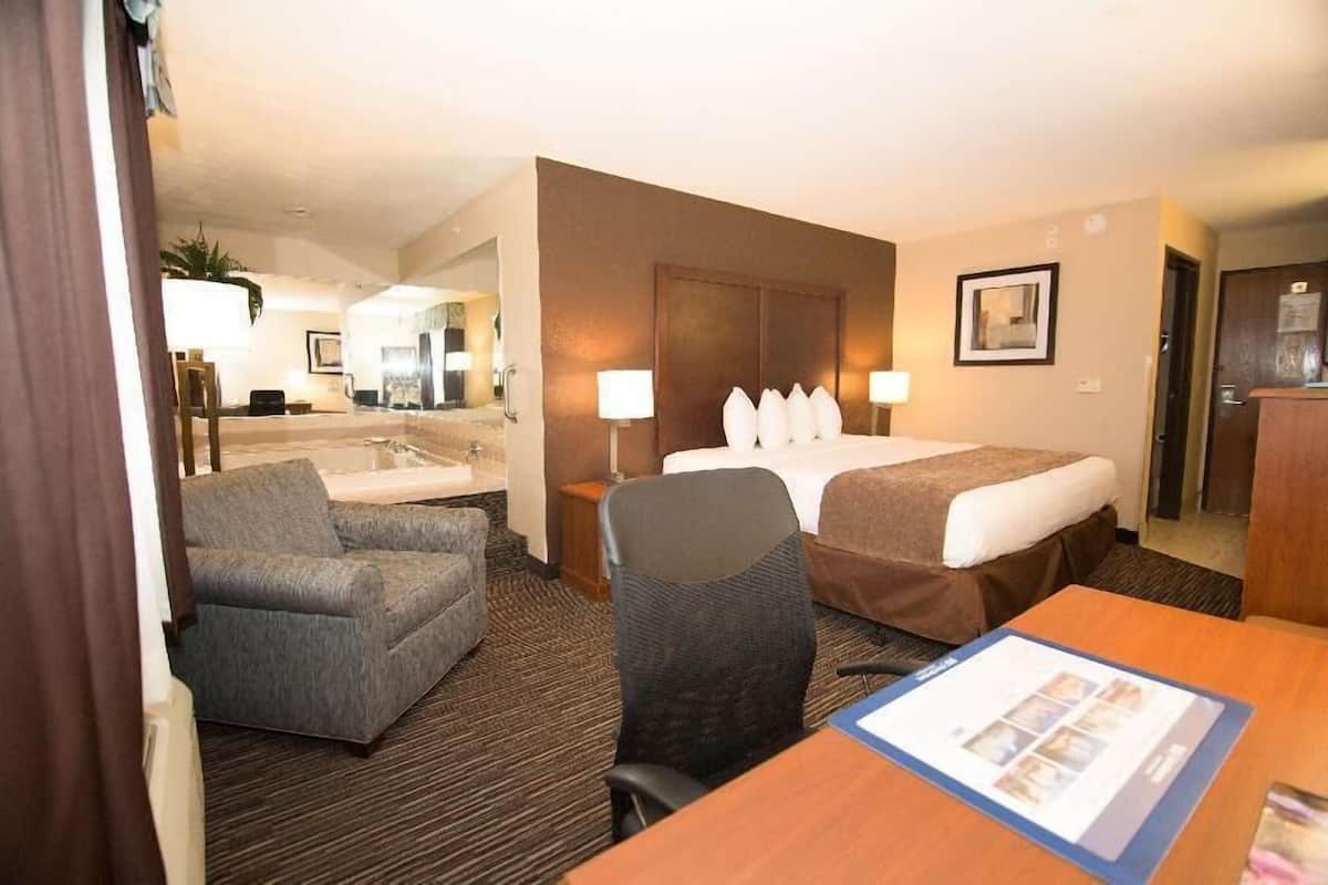 A hotel room with a bed, a desk, a chair, a sofa, a bathroom, and a mirror.