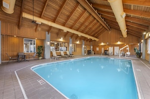 Una piscina interior con vigas de madera, sillones de descanso y suelo de baldosas.