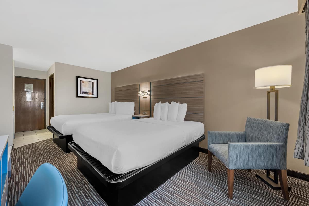 A hotel room with a large bed, a desk, a chair, and a bedside table.