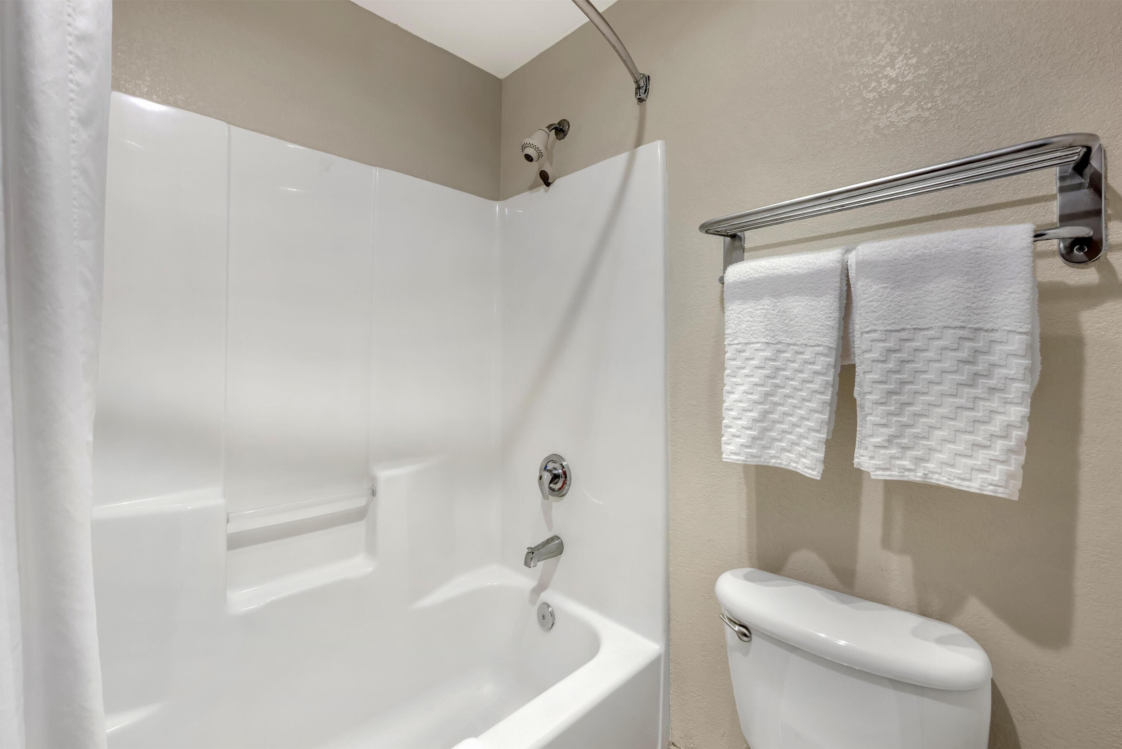 A modern bathroom with a white bathtub, a chrome showerhead, and a toilet with a towel rack above it.