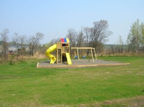 A playground with a slide and swings in a grassy field.