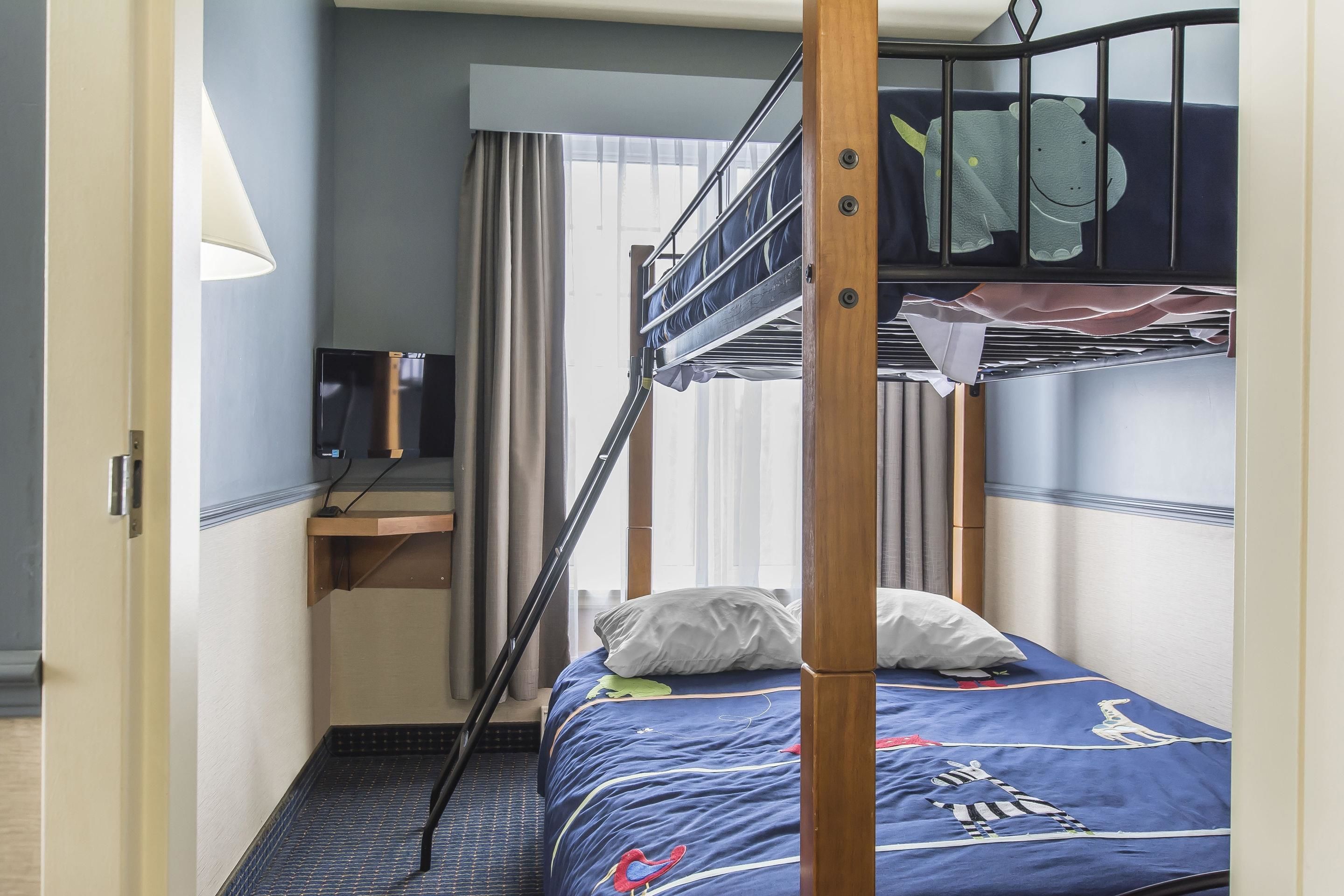 A bunk bed with a desk and a television in a room with a window and curtains.