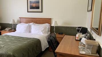 Habitación de hotel con cama, lámparas de noche, mesita de noche con teléfono, mesa con bandeja de artículos de aseo y un cuadro en la pared.